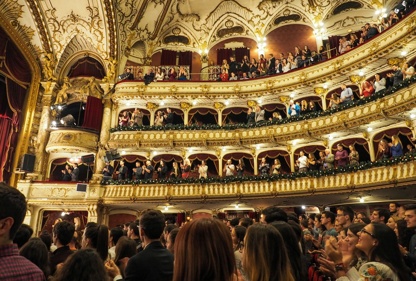 Ein begeistertes Theaterpublikum, das auf verzierten, gestuften Balkonen applaudiert.