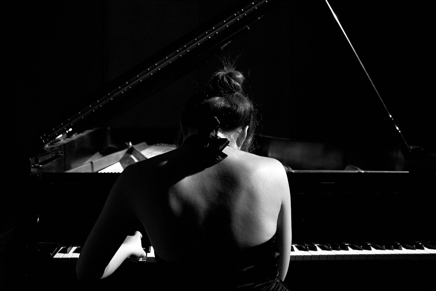 Frau spielt auf einem schwarzen Flügel, Rücken freigelegt.